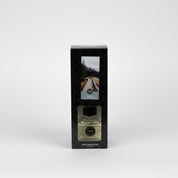 A boxed Solitude Reed Diffuser by Bridgewater Candle featuring fiber reeds and a glass bottle of premium fragrance. The packaging shows a wooden path through a forest and is labeled Reed Diffuser.