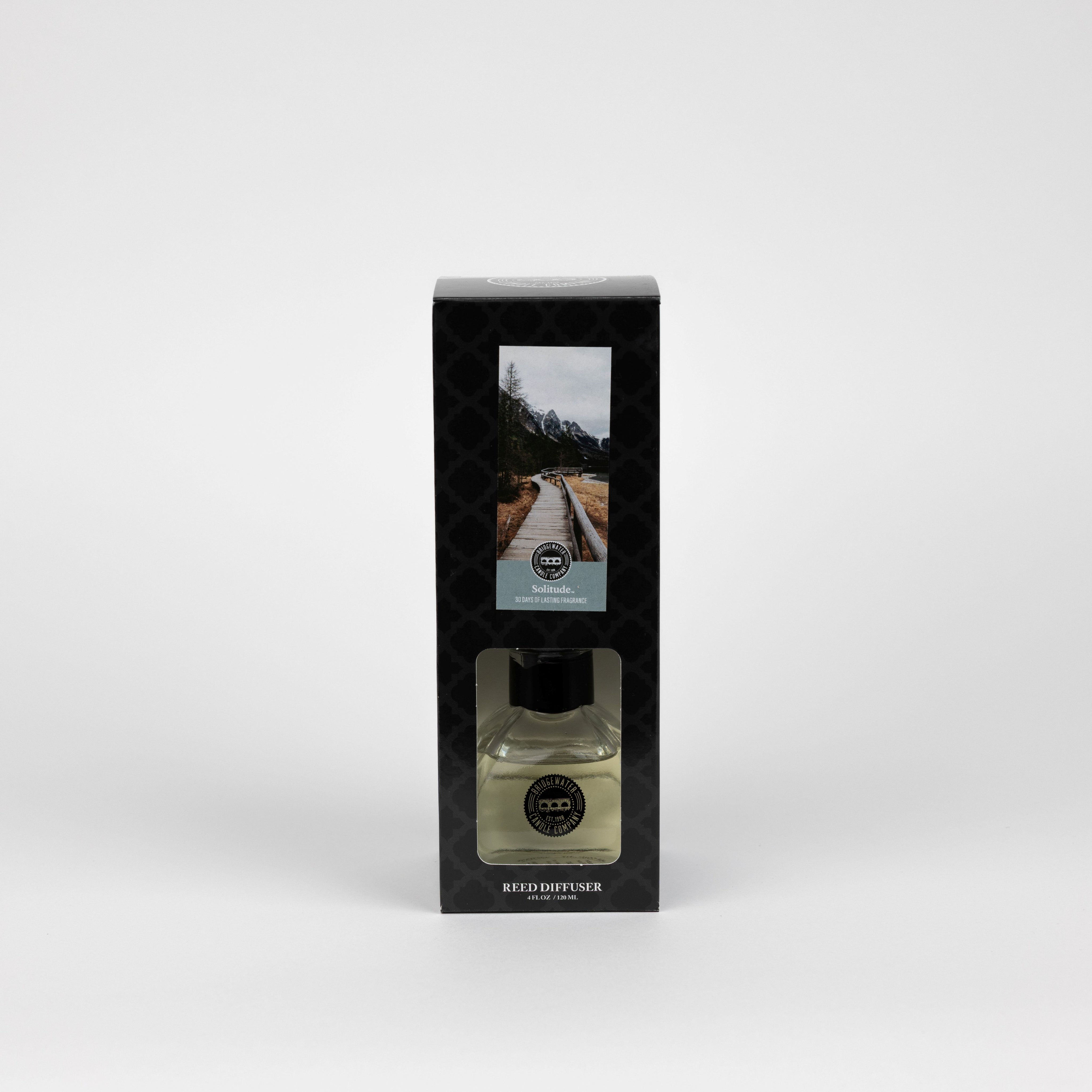 A boxed Solitude Reed Diffuser by Bridgewater Candle featuring fiber reeds and a glass bottle of premium fragrance. The packaging shows a wooden path through a forest and is labeled Reed Diffuser.