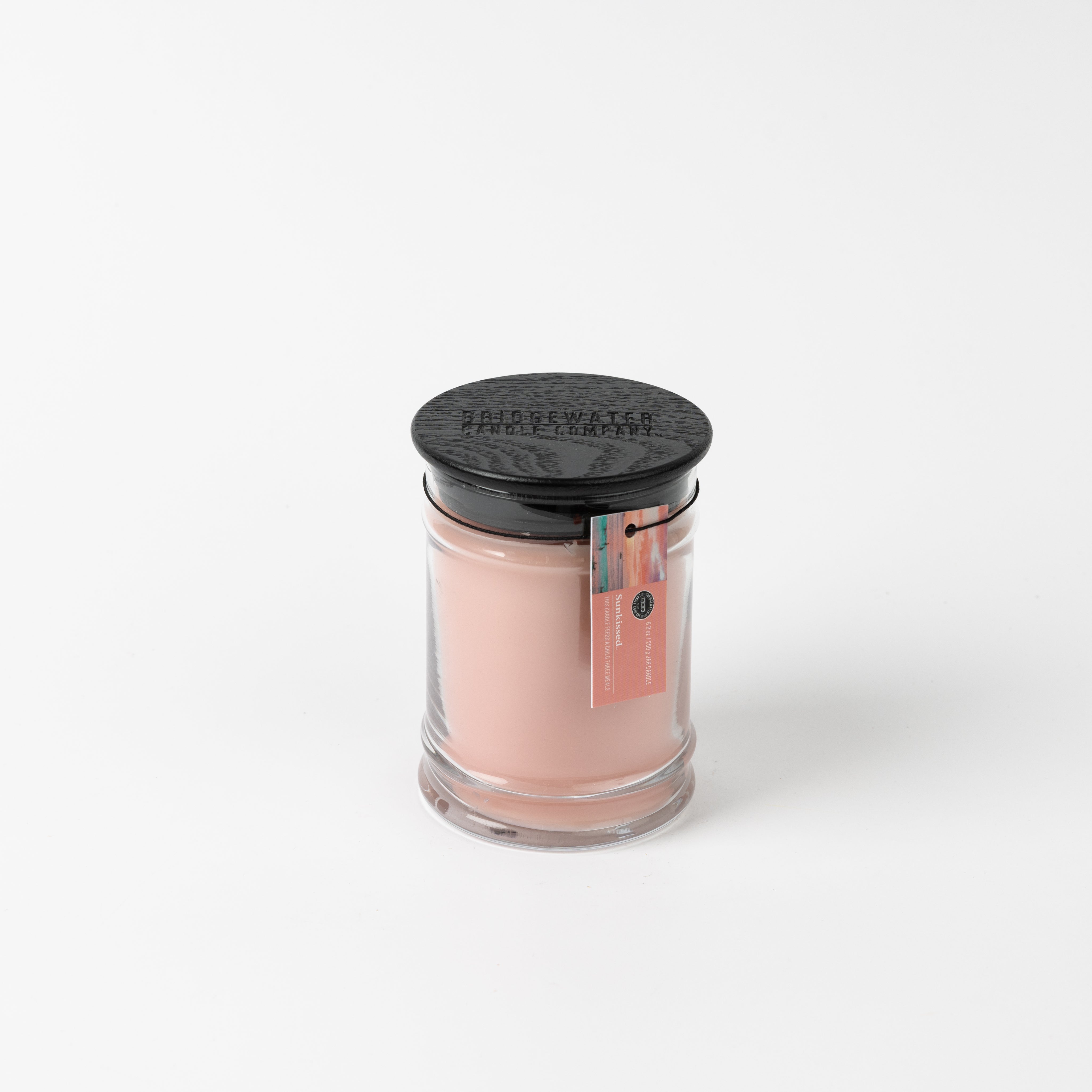 A Bridgewater Candle Sunkissed 8oz Jar Candle with light pink soy-blend wax, black lid, and a pink and green tag is shown on a white background.