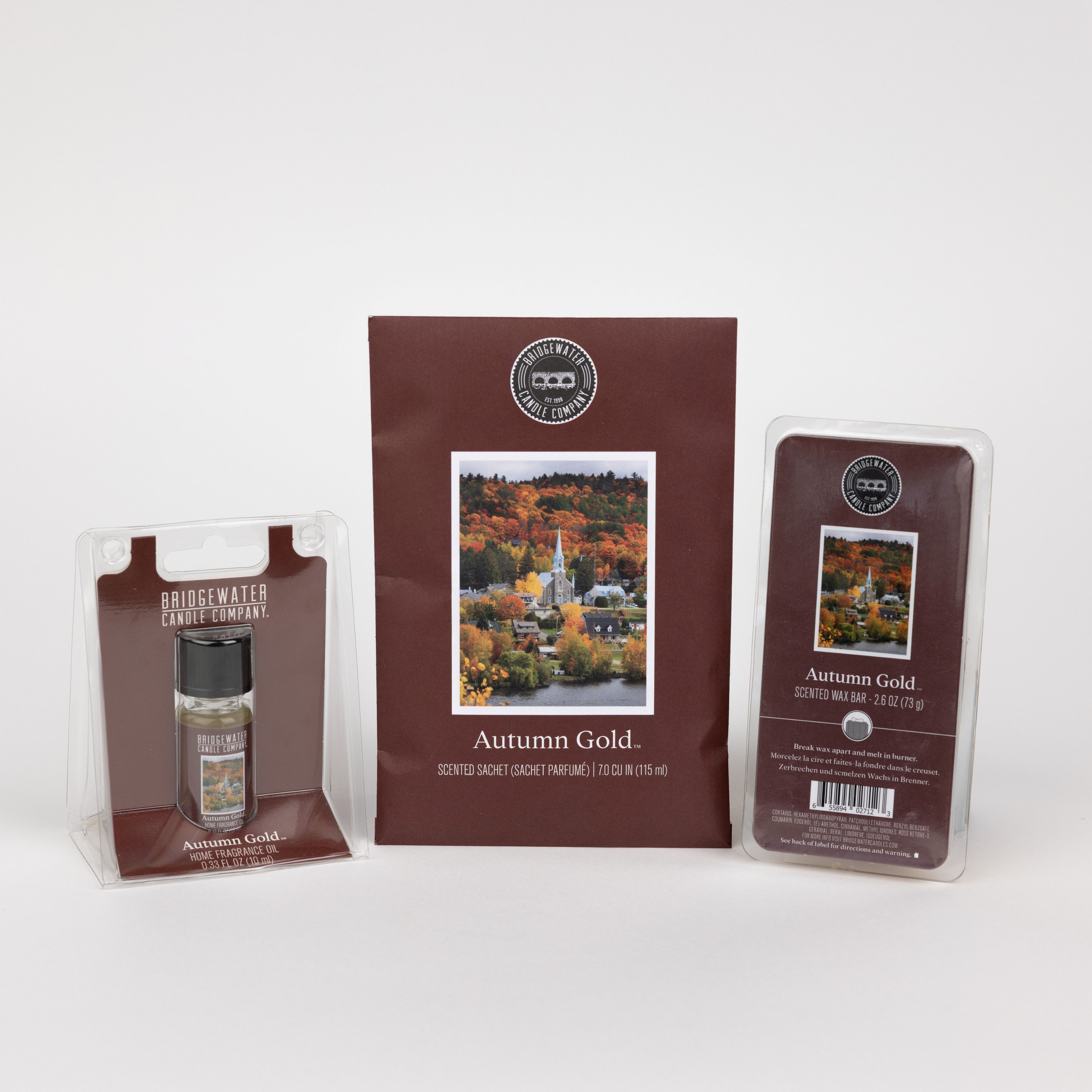 The Bridgewater Candle Autumn Gold Flameless Bundle includes a small jar candle, scented sachet, and soy-blend wax bar, each in brown packaging with autumn town imagery for a cozy fall atmosphere.