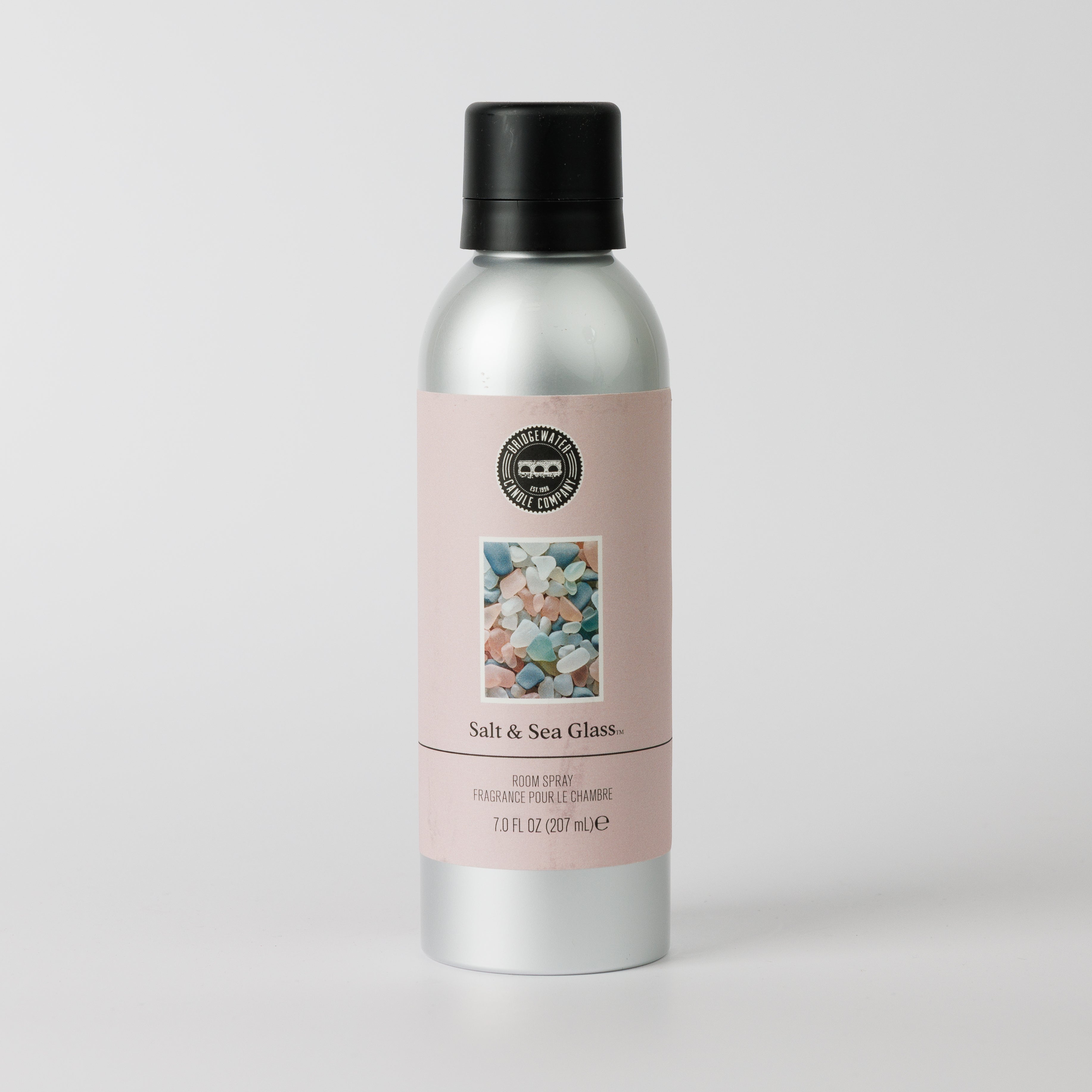 A silver 7.0 fl oz (207 ml) bottle of Bridgewater Candle’s Salt & Sea Glass Non-Aerosol Room Spray has a black cap and pink pastel sea glass label highlighting its premium fragrance.