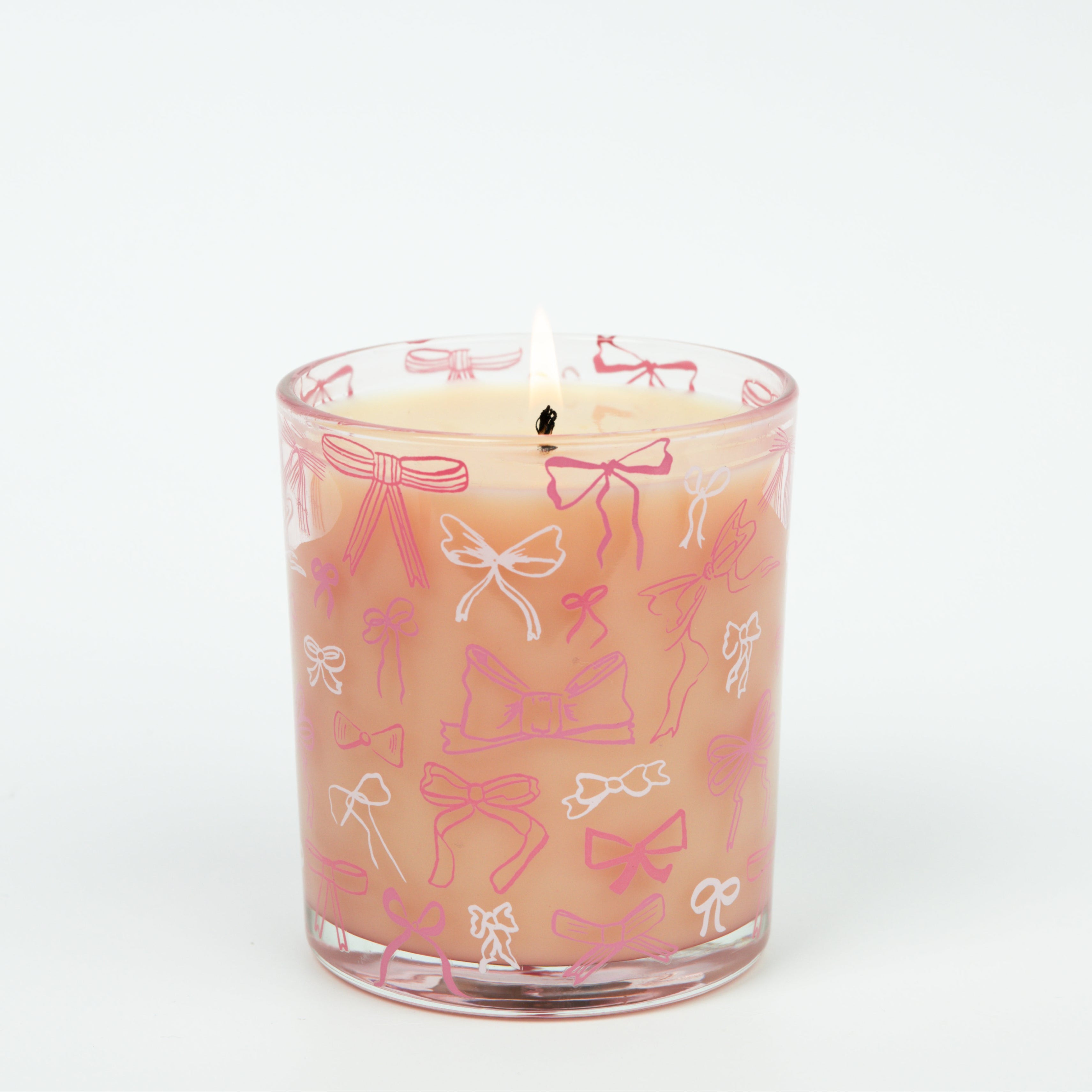 The Sweet Grace Pink Bow Candle by Bridgewater Candle features delicate white and pink bow designs on a glass holder. Made with soy-blend wax, this charming candle is displayed against a plain white background.