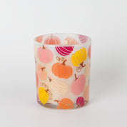 The Bridgewater Candle Sweet Grace Pumpkin Decal Candle is a white fall candle in a glass holder adorned with vibrant orange, pink, and yellow pumpkin illustrations, displayed against a plain white background.