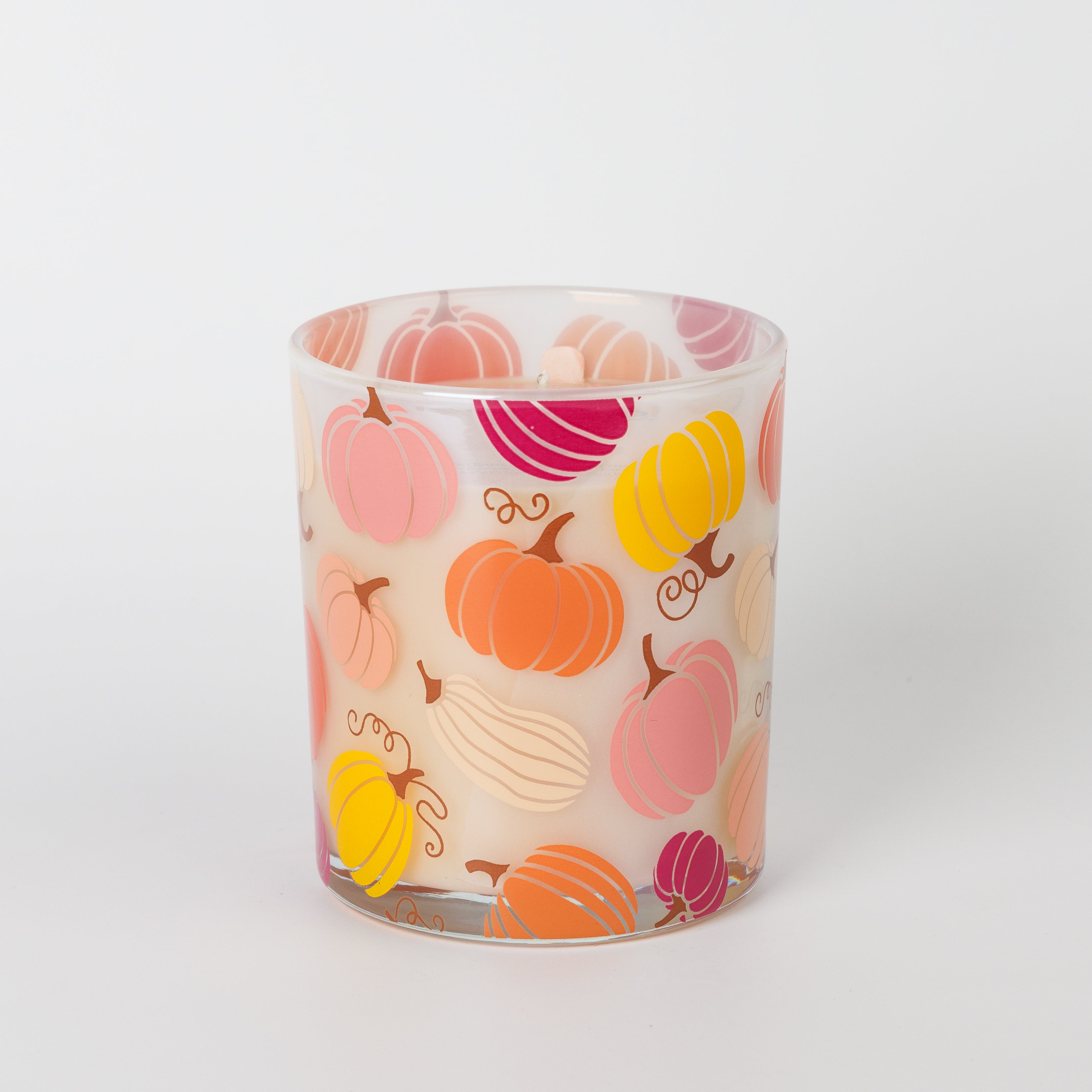 The Bridgewater Candle Sweet Grace Pumpkin Decal Candle is a white fall candle in a glass holder adorned with vibrant orange, pink, and yellow pumpkin illustrations, displayed against a plain white background.