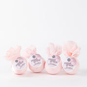 Four Bath Bomb 4 Pack-Sweet Grace by Bridgewater Candle, wrapped in light pink paper and featuring the best-selling Sweet Grace scent, are lined up against a plain white background.