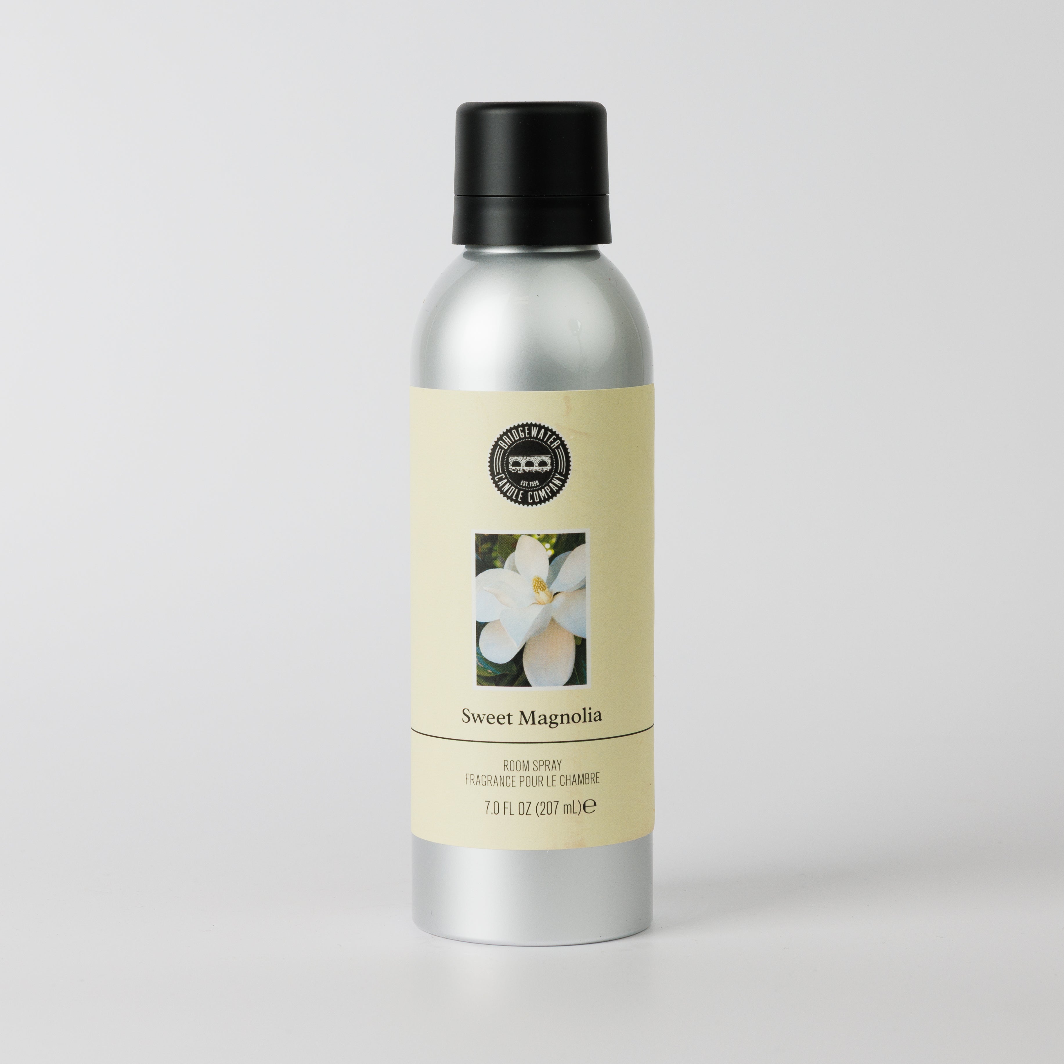 A silver bottle of Bridgewater Candle’s Sweet Magnolia Non-Aerosol Room Spray with a black cap, featuring a magnolia flower label on a light background, offers a premium fragrance experience.