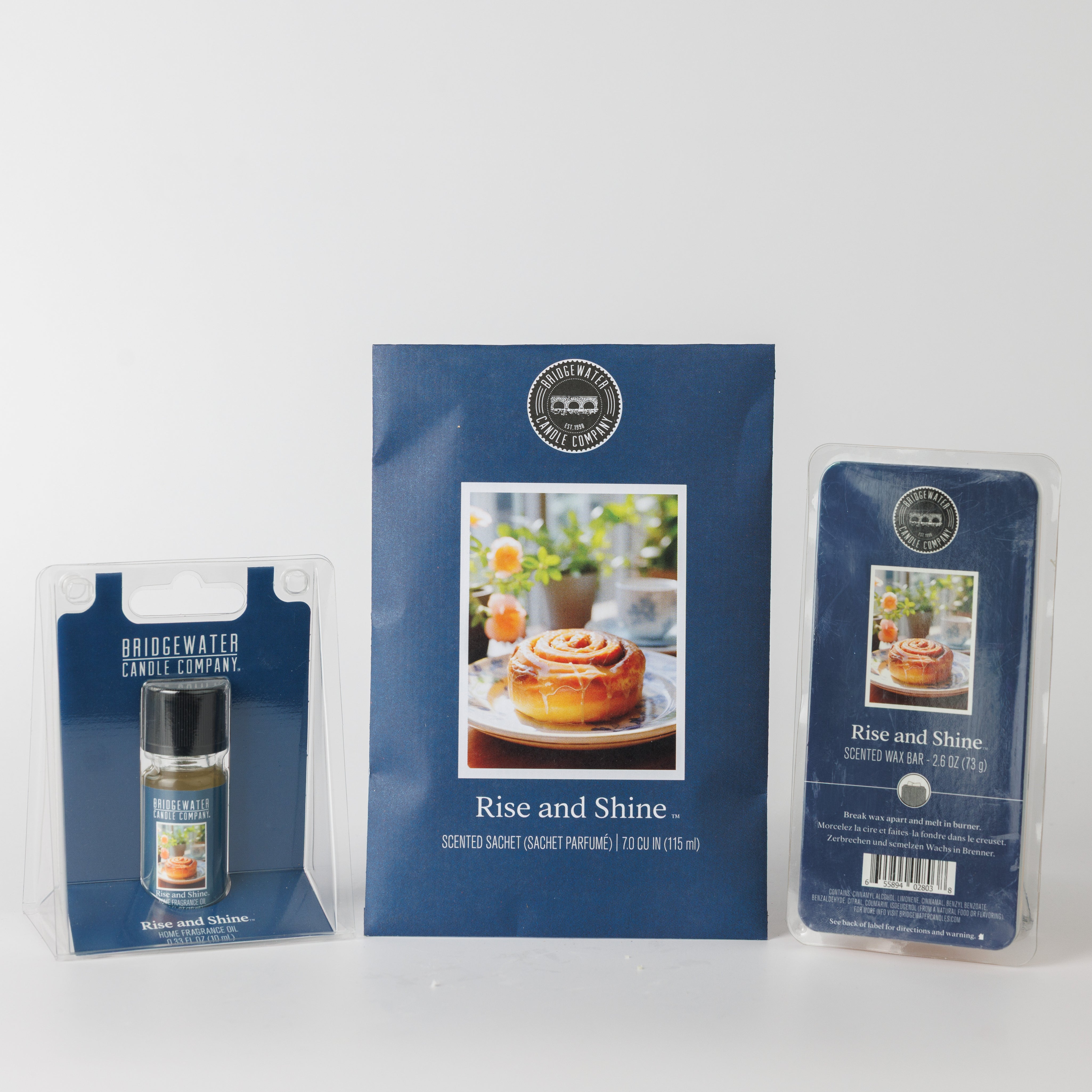 The Bridgewater Candle Rise & Shine Flameless Bundle features a home fragrance oil, scented sachet, and wax bar in blue packaging with a cinnamon roll image, all displayed on a white background.