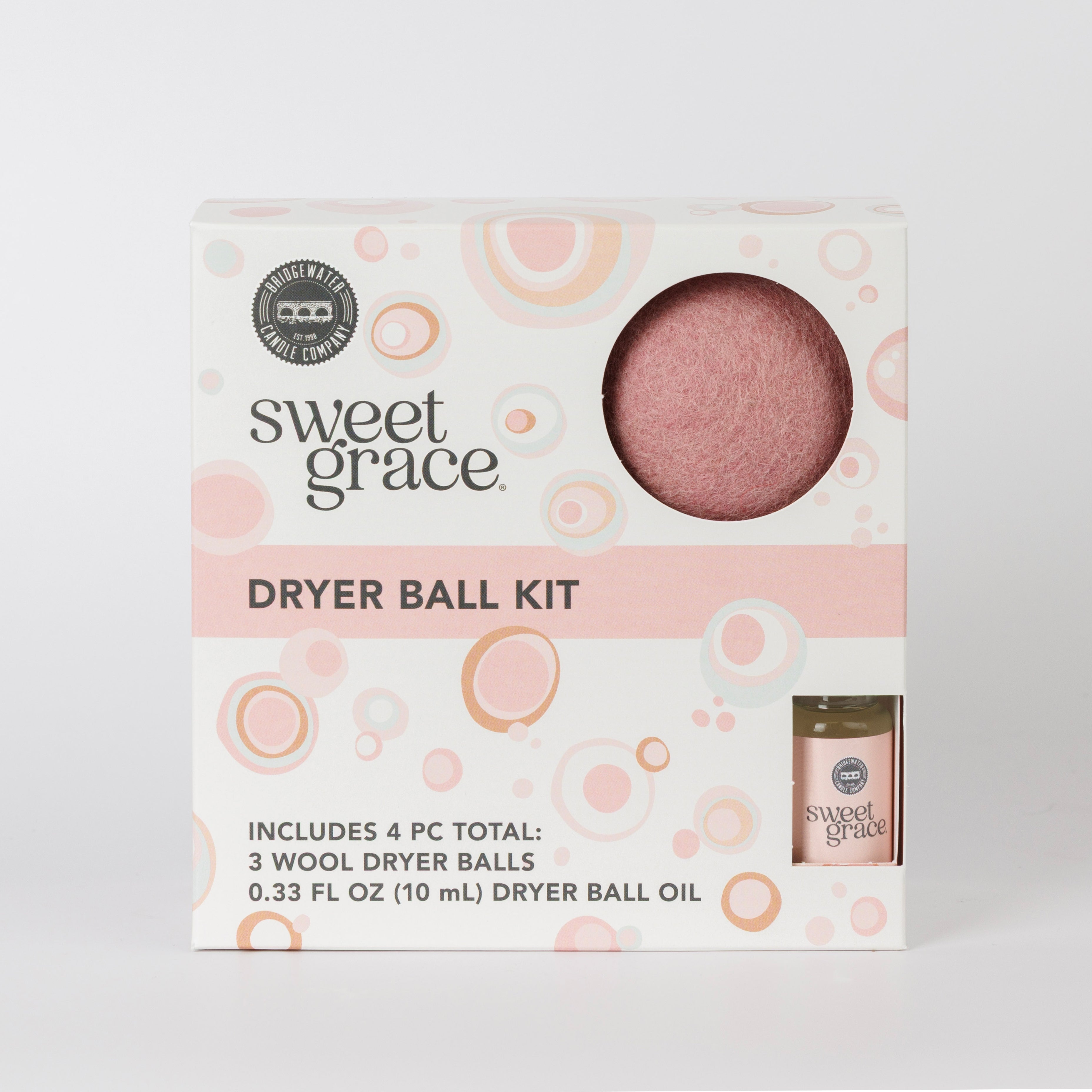 The Bridgewater Candle Sweet Grace Dryer Ball Kit features a box with a circular window, revealing pink wool dryer balls. It includes 3 dryer balls, a 0.33 fl oz (10 mL) fragrance oil, and packaging with pink and orange circles.