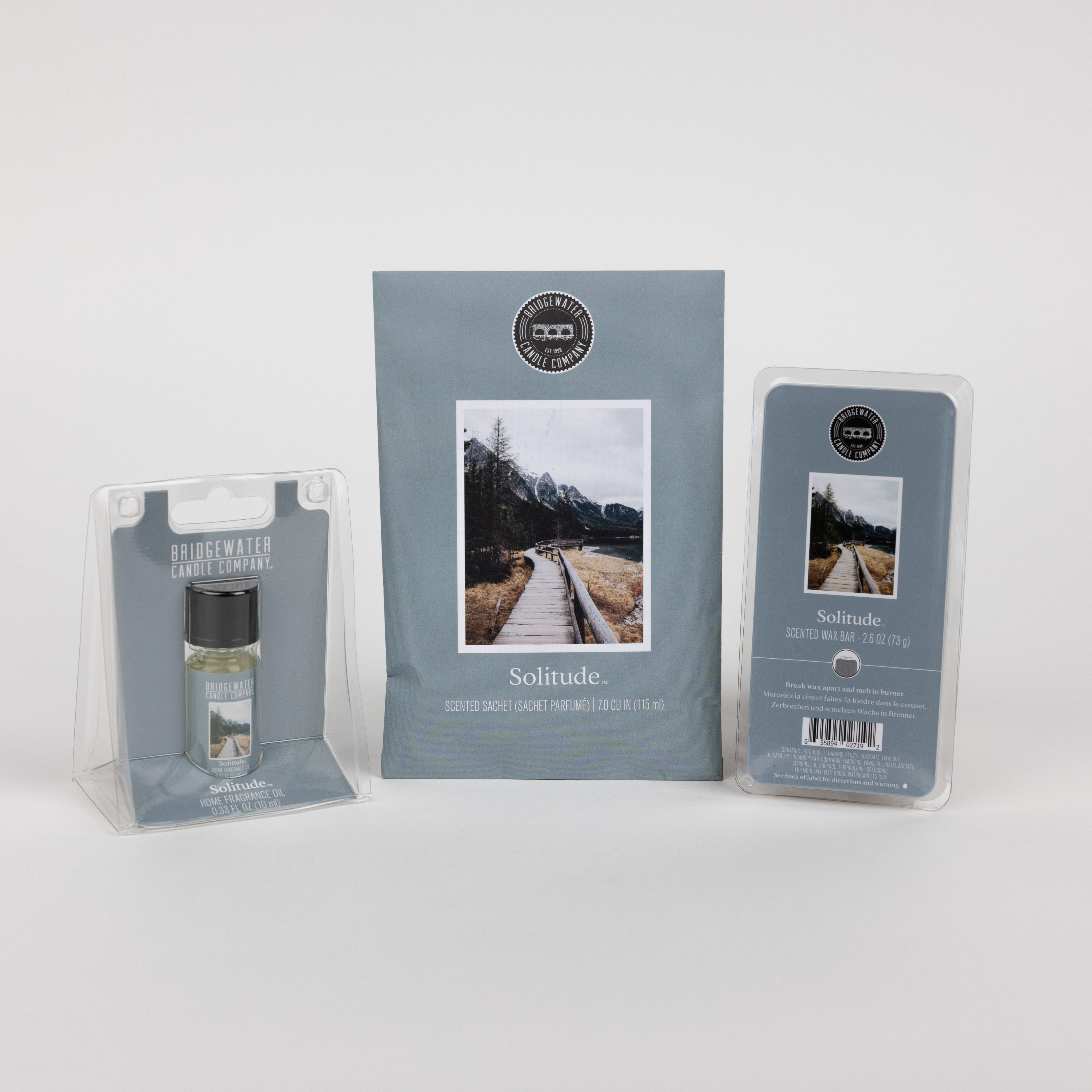 The Solitude Flameless Bundle by Bridgewater Candle includes a room spray, scented sachet, and wax melts, each packaged with a photo of a wooden pathway leading toward mountains.