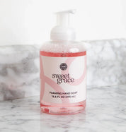 A clear plastic bottle of Fast Bundle’s Sweet Grace Foam & Pamper Bundle with pink liquid sits on a marble counter. The white pump pairs perfectly with the matching hand cream for a complete care set.