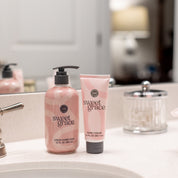The Sweet Grace On Hand Bundle—featuring Hand Cream & Liquid Hand Soap—rests on a bathroom countertop by the sink, with a glass jar and mirror behind, perfect for an elevated hand care routine.