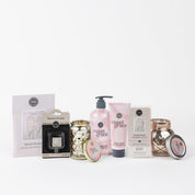 The Sweet Grace Lucky 7 Bundle includes candles, hand soap, hand cream, wax melt, sachet, and a small tin in elegant pink, white, and gold packaging arranged on a white background.
