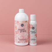 Two pink bottles from the Sweet Grace Laundry Bundle stand on a pink surface, with Sweet Grace Laundry Detergent on the left and Wrinkle Release Spray on the right, both featuring circular patterned labels.