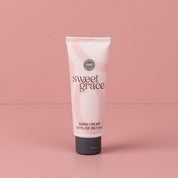 A pink tube of Sweet Grace hand cream with a gray cap stands upright on a pink background, perfectly complementing the foaming hand soap in the Sweet Grace Foam & Pamper Bundle by Fast Bundle.