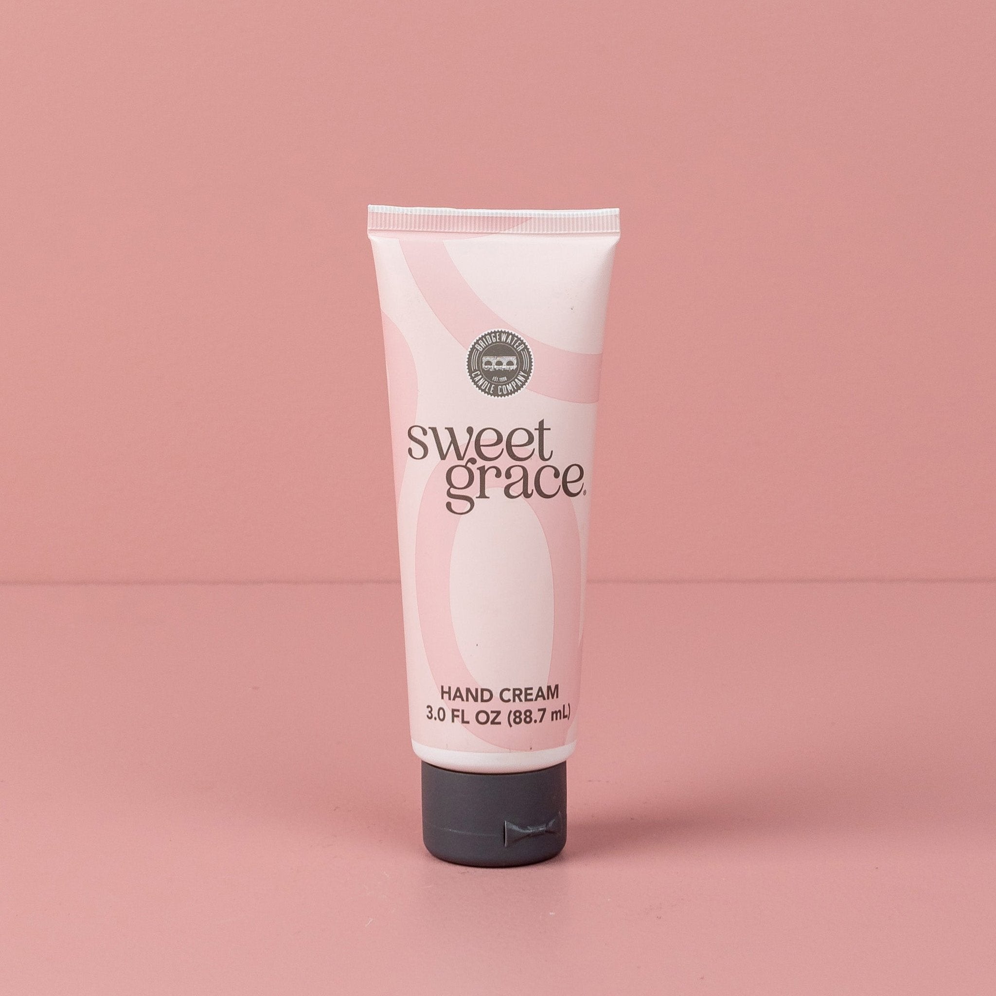 A pink tube of Sweet Grace hand cream with a gray cap stands upright on a pink background, perfectly complementing the foaming hand soap in the Sweet Grace Foam & Pamper Bundle by Fast Bundle.