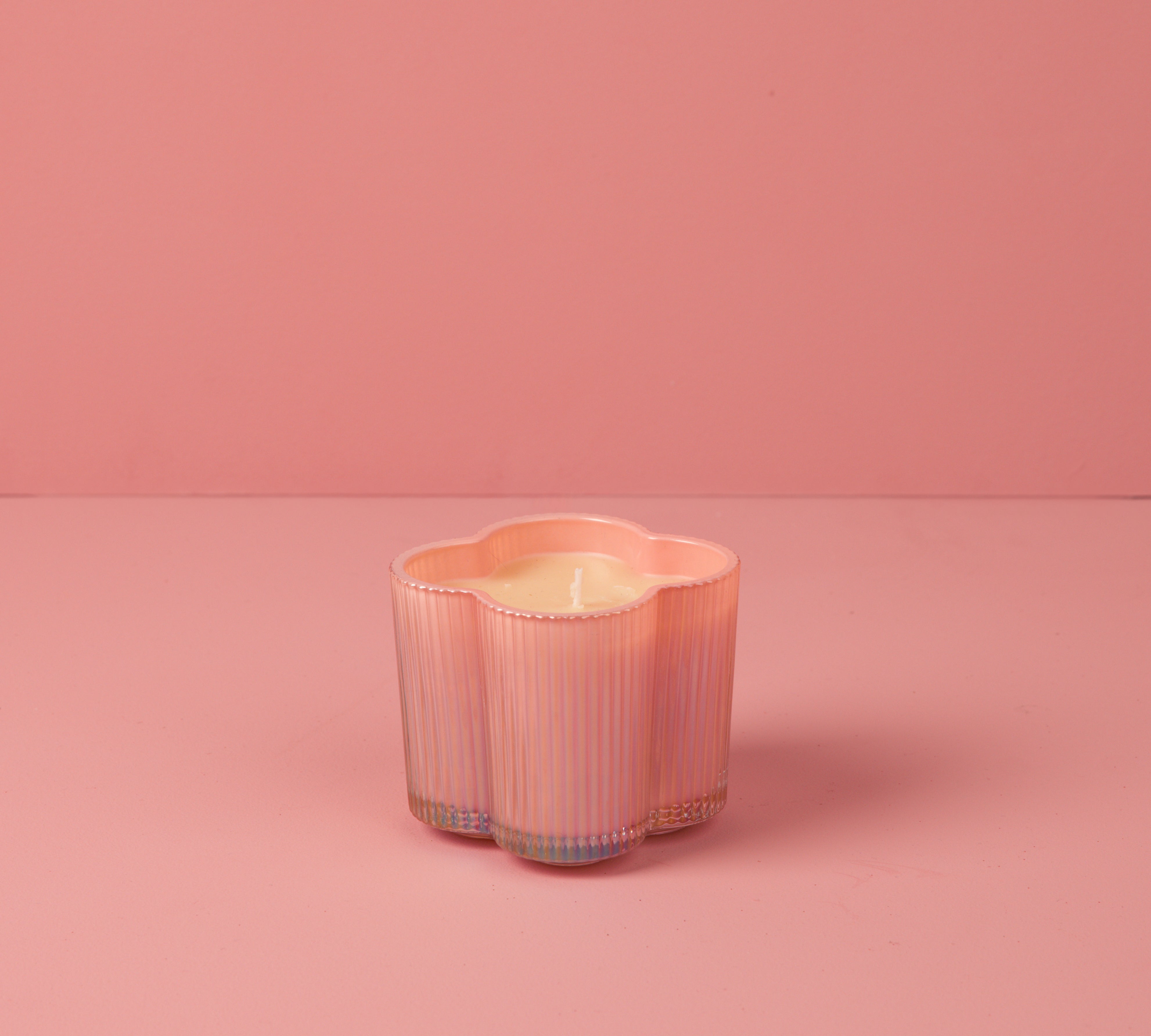 The Sweet Grace Collection Candle #075 by Bridgewater Candle features a flower-shaped, pink iridescent vessel on a matching surface and background. Made from soy-blend wax, it offers a clean, gentle glow with a soft, monochromatic look.