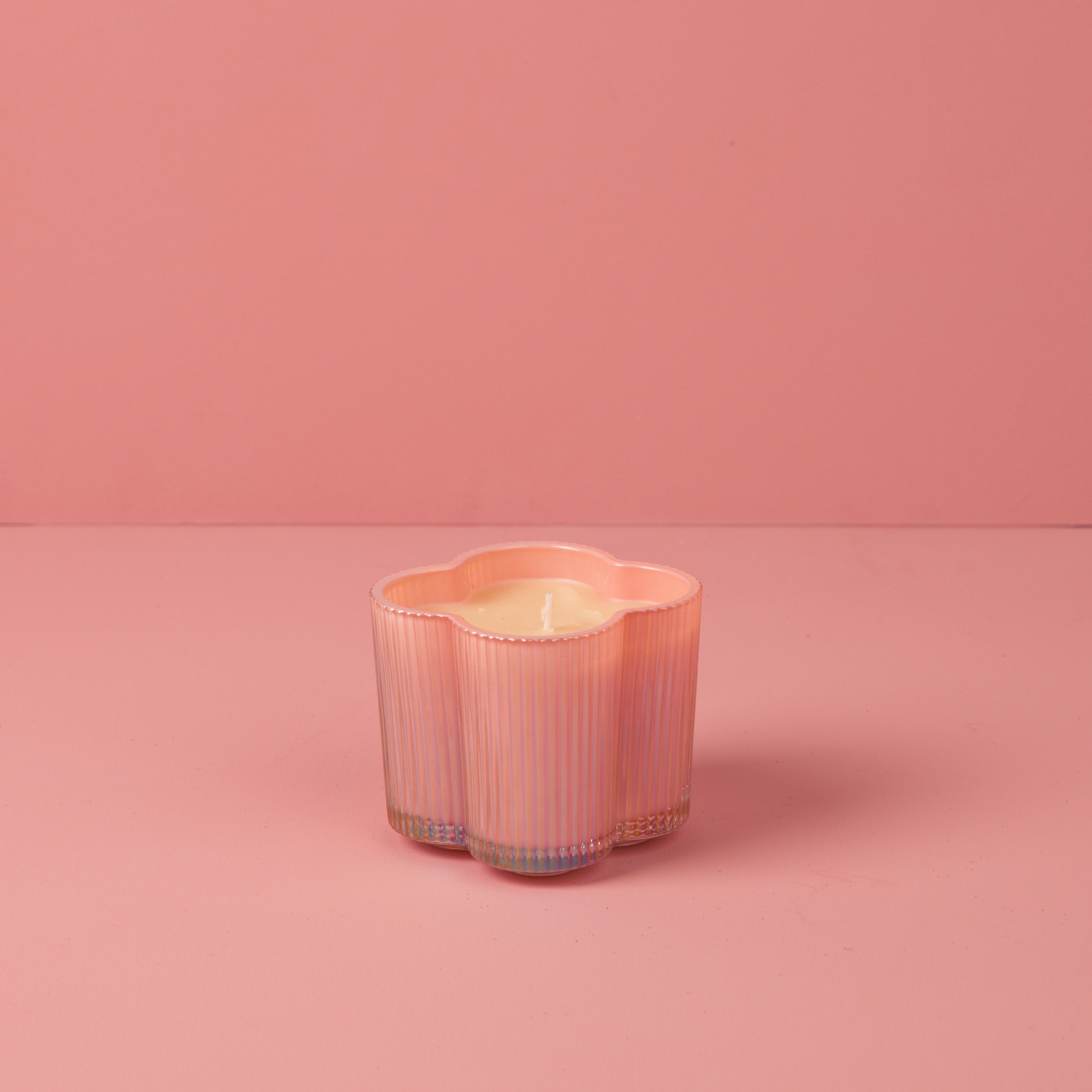 The Sweet Grace Collection Candle #075 by Bridgewater Candle features a flower-shaped, pink iridescent vessel on a matching surface and background. Made from soy-blend wax, it offers a clean, gentle glow with a soft, monochromatic look.