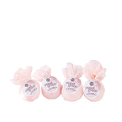 A set of four Sweet Grace bath bombs by Bridgewater Candle, wrapped in pink tissue and tied at the top, are beautifully arranged in a row against a white background.