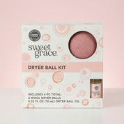 A Bridgewater Candle Sweet Grace Dryer Ball Kit box sits against a pink background, displaying 3 wool dryer balls (one visible through a window) and a small bottle of fragranced oil. The white packaging features pink and orange circle designs.