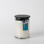 The Bridgewater Candle "I'll Be Home" 8oz jar candle features white soy-blend wax, a black lid, and a blue rectangular label with brand imagery on the neck. It stands against a white background.