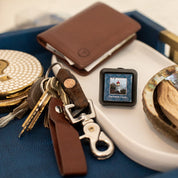 A square Auto Vent Clip-Nantucket Coast air freshener featuring a lighthouse, resting on a tray next to a set of keys and a wallet.