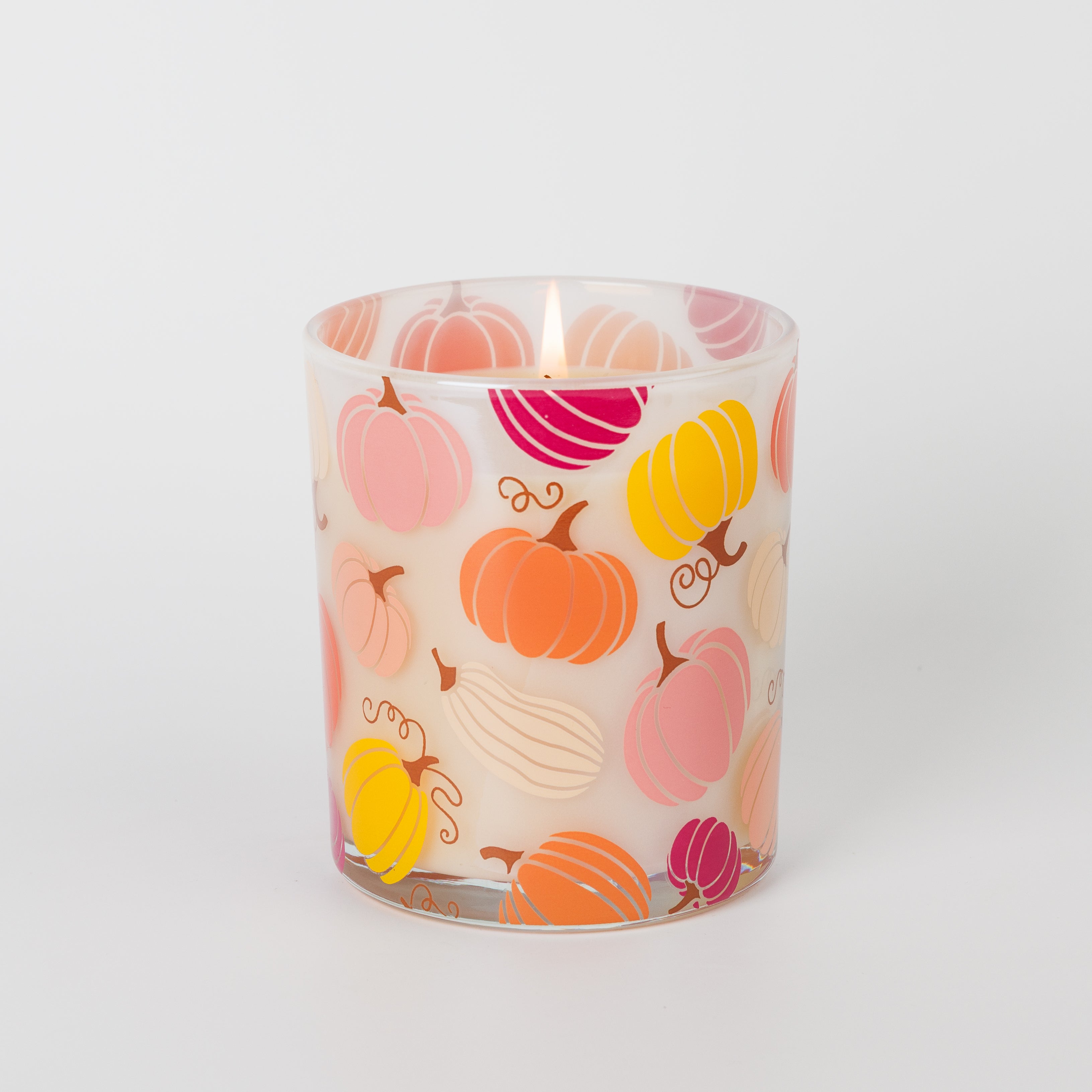 The Sweet Grace Pumpkin Decal Candle by Bridgewater Candle glows in a glass holder adorned with colorful pumpkin illustrations in shades of orange, pink, yellow, and cream, set against a plain white background—making it the perfect Thanksgiving candle to enhance your fall décor.