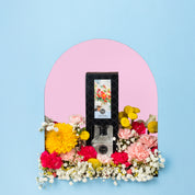 The High Bloom Reed Diffuser by Bridgewater Candle is showcased in an arched alcove with a pink background, accented by colorful flowers against a light blue wall for a charming home décor and premium fragrance experience.
