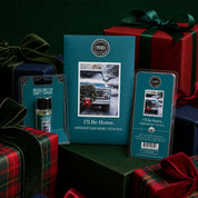 Bridgewater Candle’s "I’ll be Home Flameless Bundle" is showcased with winter-themed packaging featuring a vintage truck and wreath, alongside wrapped holiday gifts in the background.