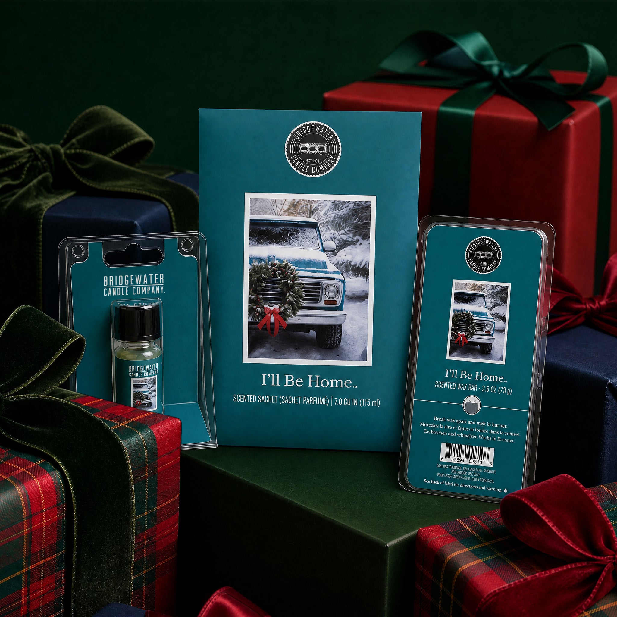 Bridgewater Candle’s "I’ll be Home Flameless Bundle" is showcased with winter-themed packaging featuring a vintage truck and wreath, alongside wrapped holiday gifts in the background.