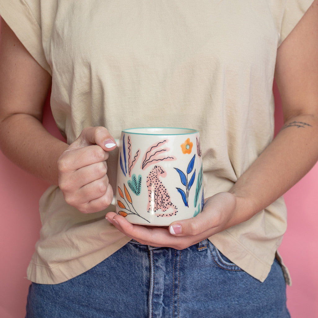 A person in a beige shirt and blue jeans holds the Bridgewater Candle Company Sweet Grace Collection Candle #048 against a pink background.