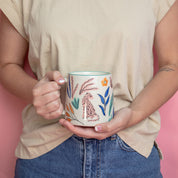 A person in a beige shirt and blue jeans holds the Bridgewater Candle Company Sweet Grace Collection Candle #048 against a pink background.